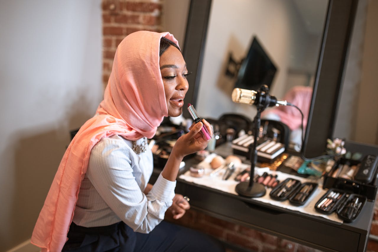 story-01 Muslim woman in pink hijab applying makeup while recording a beauty vlog indoors.